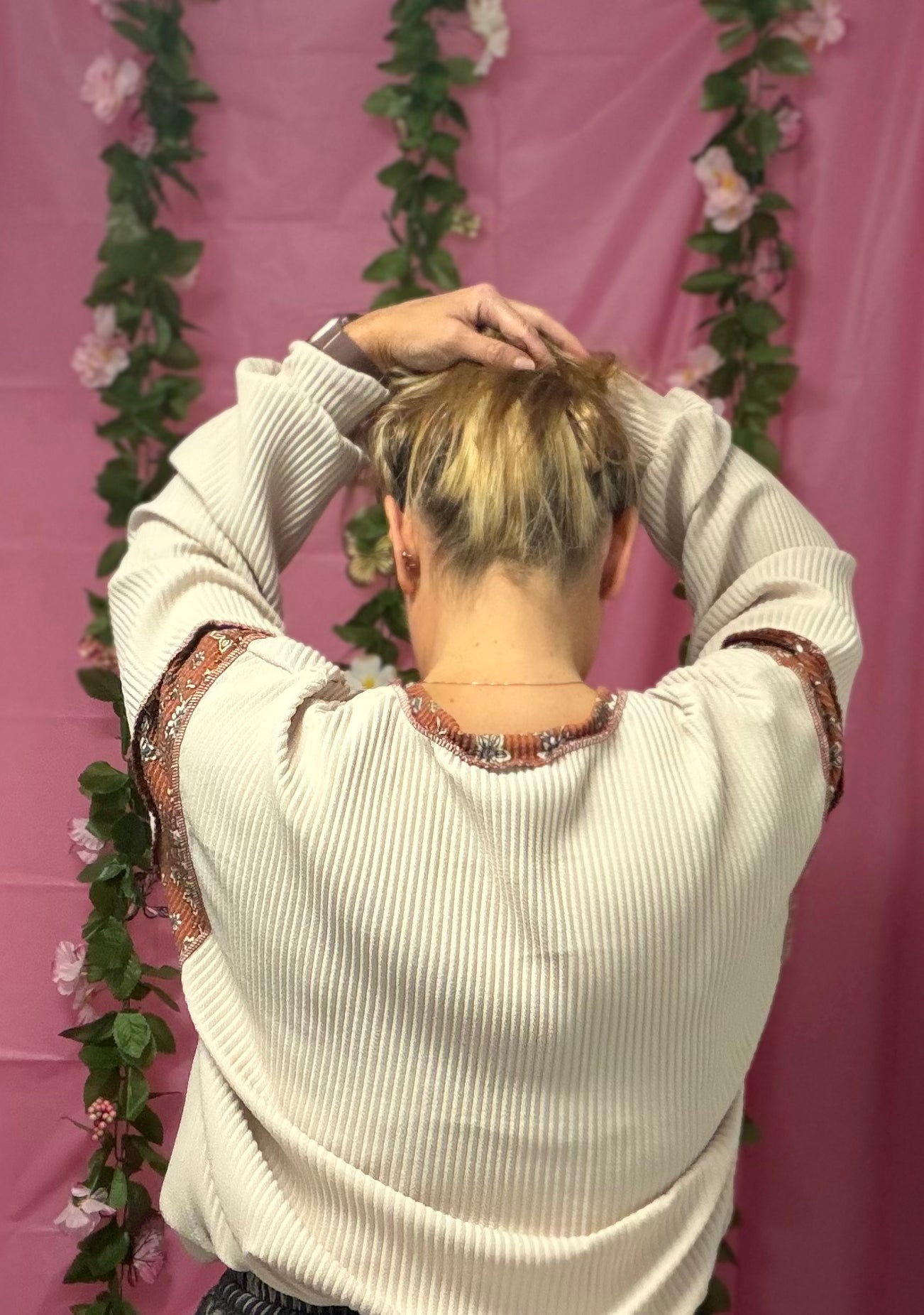 Person adjusting hair in front of a pink backdrop with floral decorations