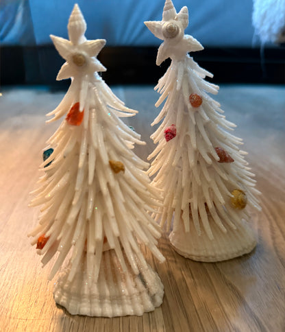 Two decorative Christmas trees made from seashells on a wooden surface.
