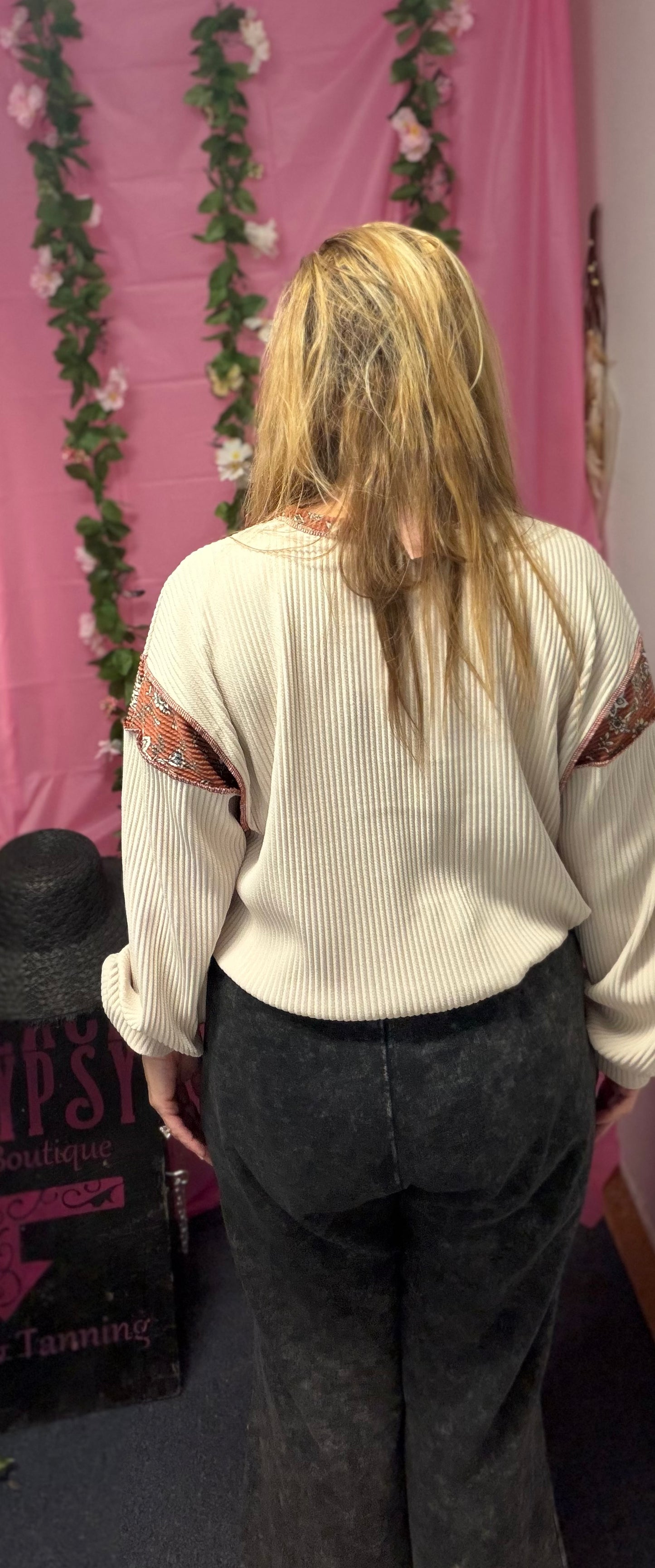 Person wearing a beige sweater with floral arm patches in front of a pink backdrop