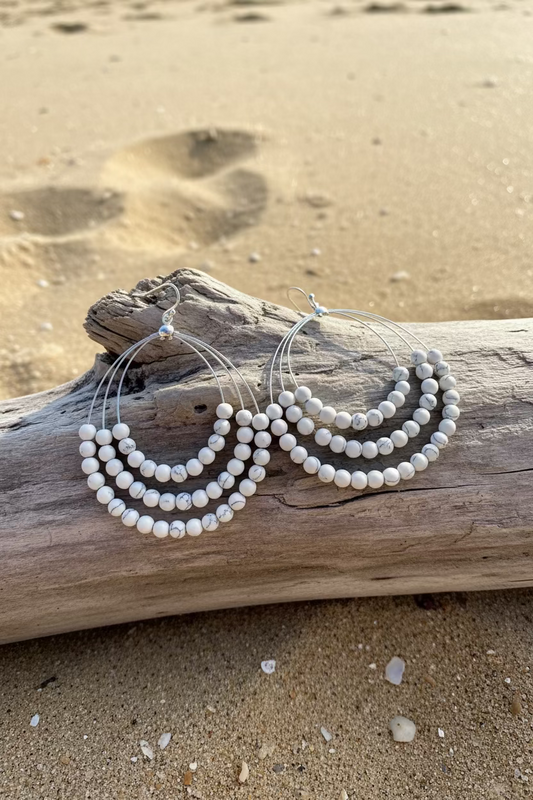 White turquoise dangle earrings on branch in beach