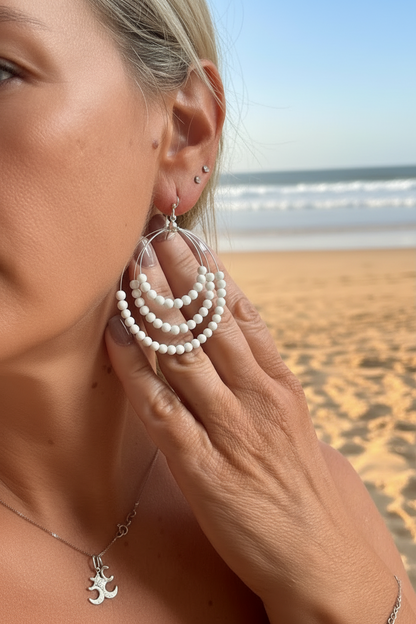 Woman wearing white beaded earrings on a beach background 
