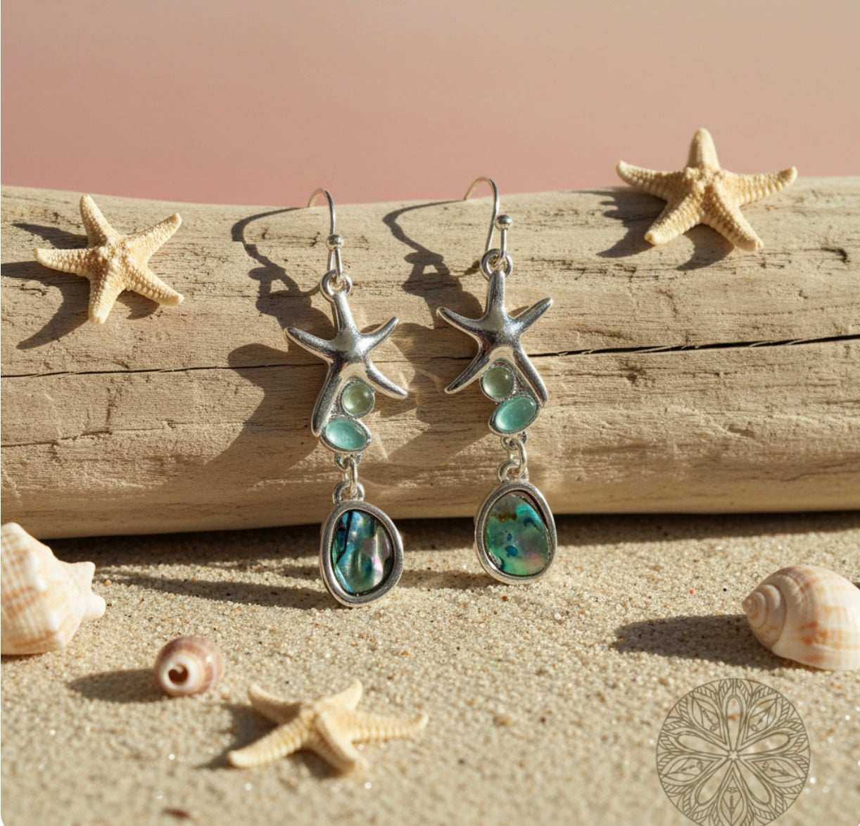 Starfish-shaped earrings with abalone and sea glass stones on a beach-themed background with starfish and shells.
