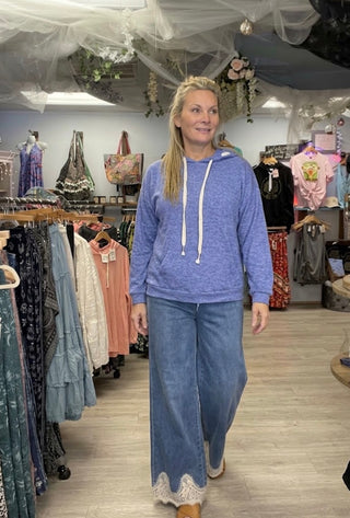 A woman wearing a heathered periwinkle blue hoodie and matching wide-leg jeans with lace trim at the hems