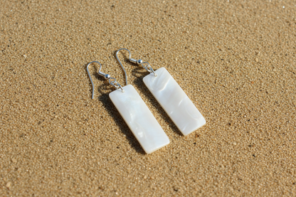 White rectangular earrings on sandy beach
