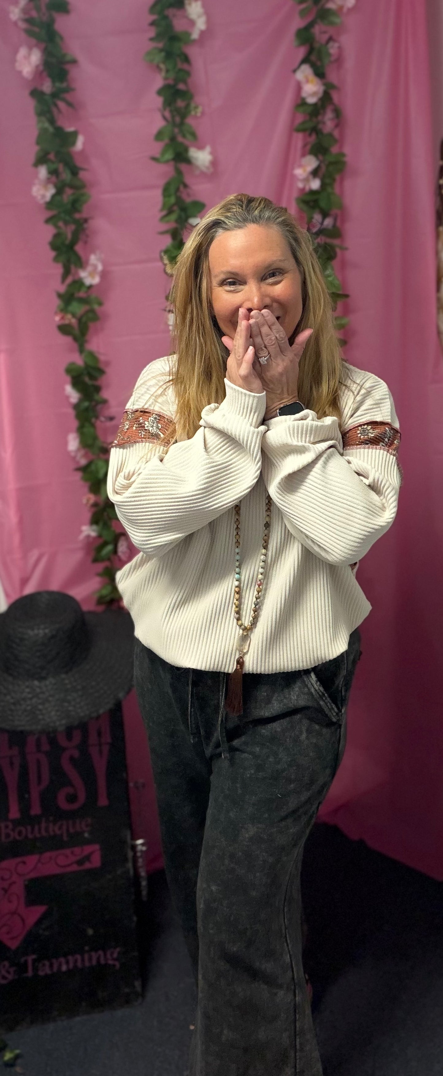 Woman posing with hands over mouth in front of a pink floral backdrop