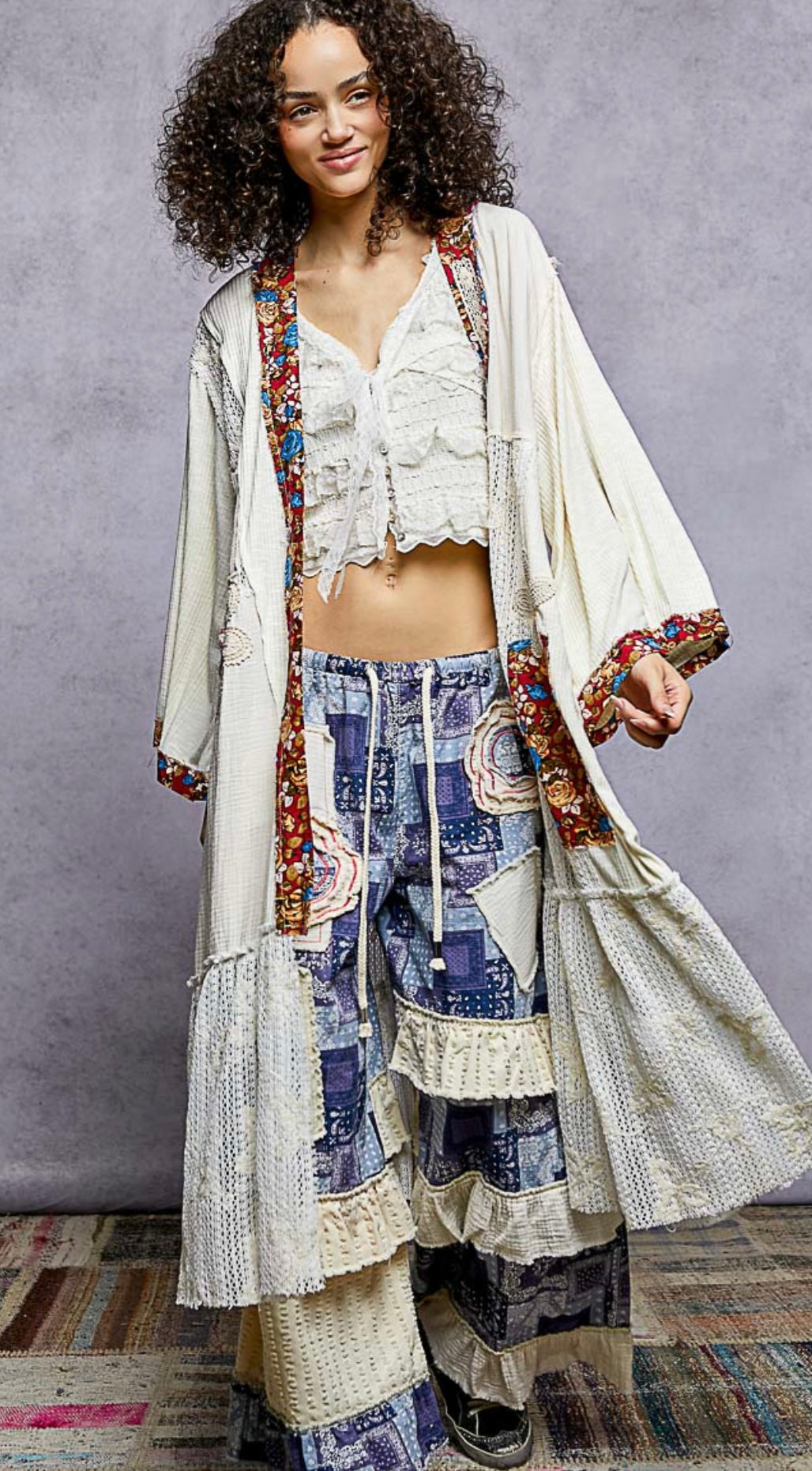 Woman wearing a stylish outfit with a long, patterned coat over a colorful dress against a gray background.