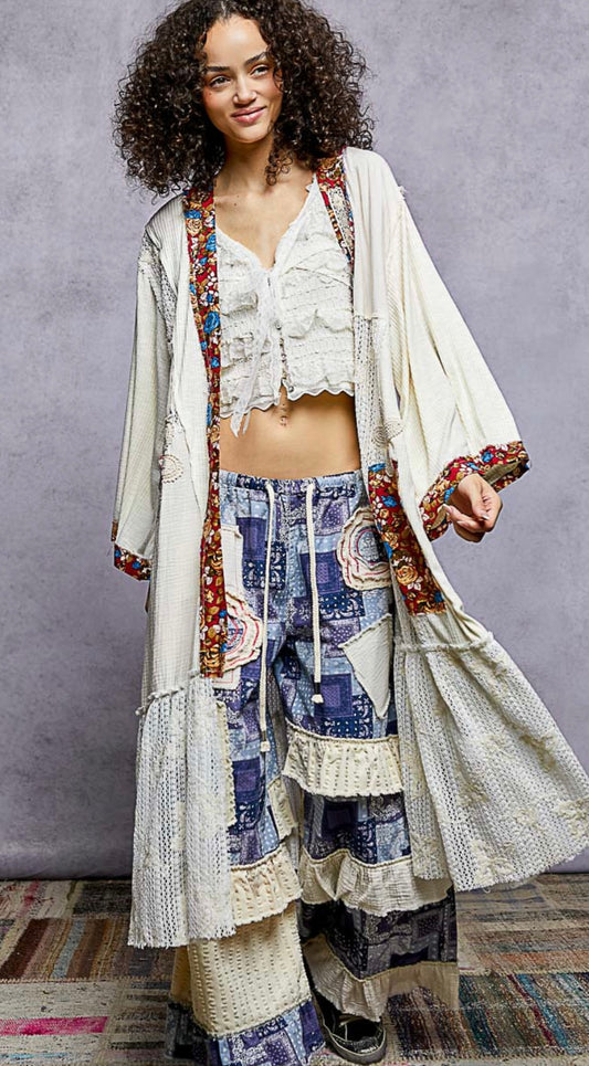 Woman wearing a stylish outfit with a long, patterned coat over a colorful dress against a gray background.