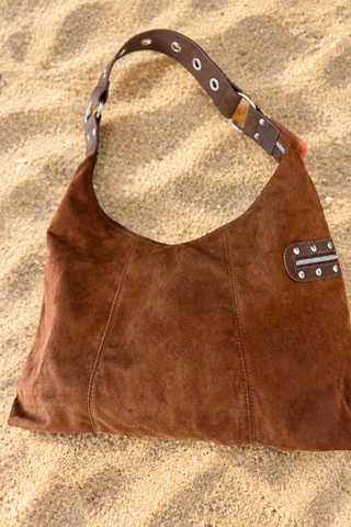 A brown suede hobo shoulder bag with brown leather trim and silver-tone metal studs and grommets
