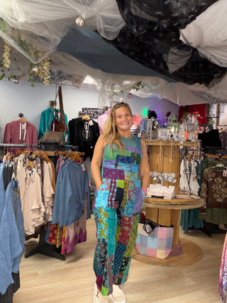 Front view of a smiling woman in a sleeveless patchwork jumpsuit in teal, pink and green prints at Beach Gypsy