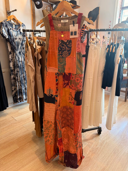 Patchwork overalls hanging in a clothing store with other garments in the background.