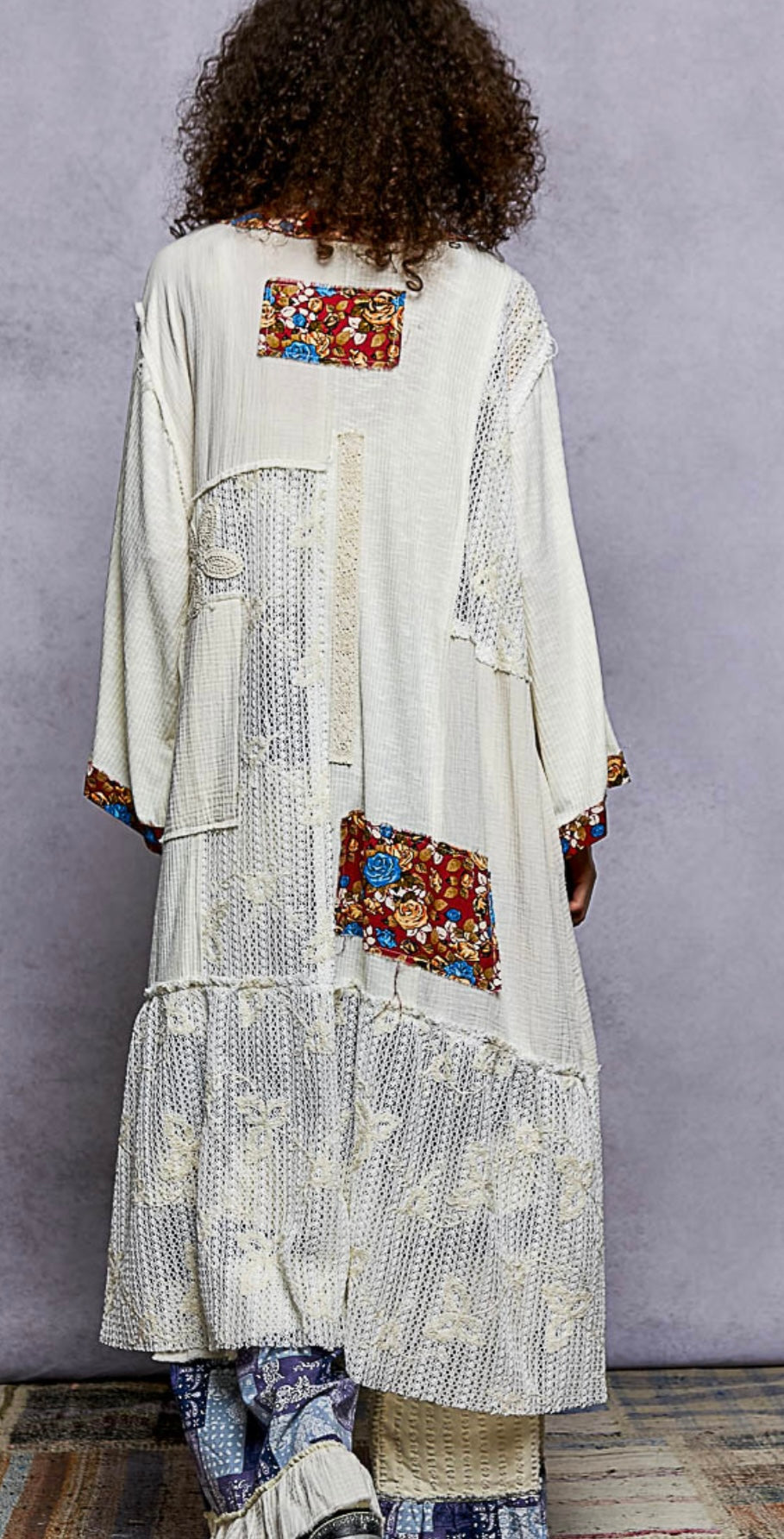 Person wearing a long, patterned dress with a textured overlay against a gray background