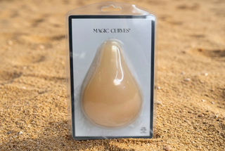 A teardrop-shaped silicone breast implant in a peach-beige color, packaged in a clear blister pack with a white backing card labeled 'MAGIC CURVES'.