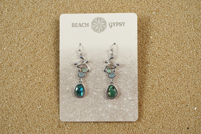 Abalone and turtle dangle earrings in a Beach Gypsy branded card on beach