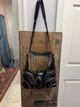 Badass Babe Studded Handbag in black with gold-tone studs, buckle detail and shoulder strap, hanging on a rustic wood door – Beach Gypsy