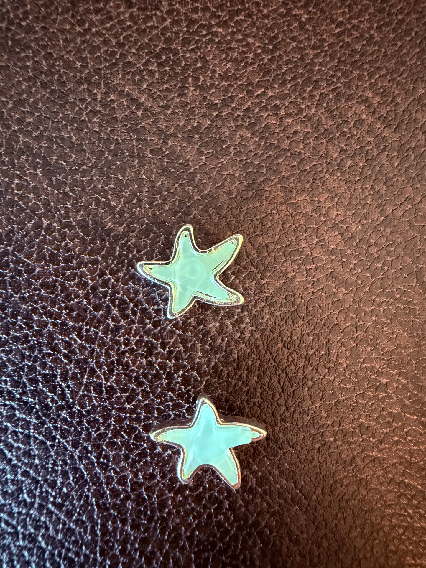 Two turquoise star-shaped earrings on a brown leather surface
