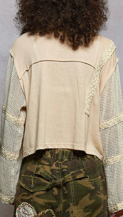 Person wearing a beige top with lace details and camouflage pants against a gray background