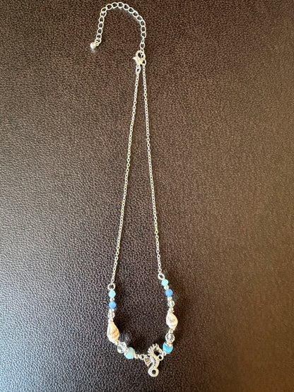 Seahorse and shell Necklace with blue beads and silver chain on a brown textured background