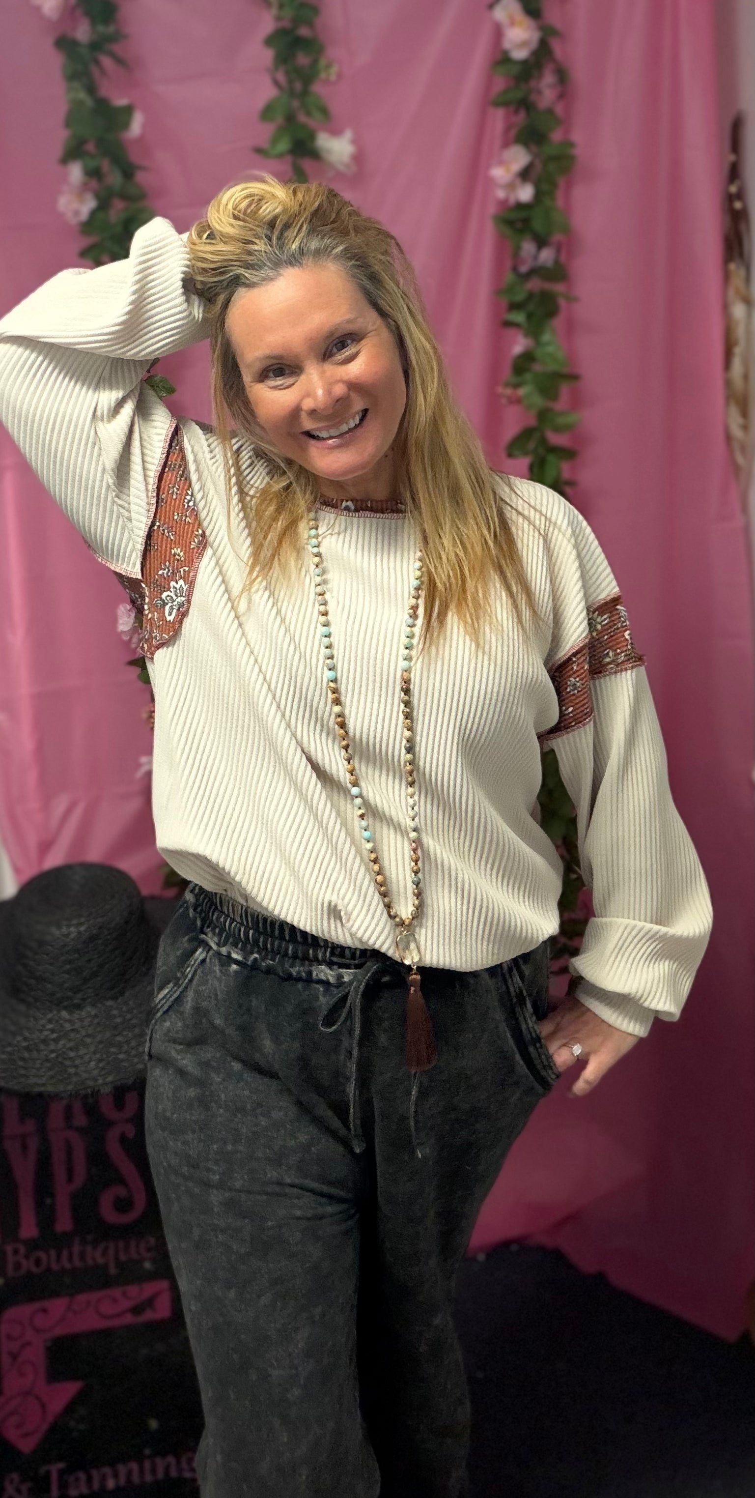 Woman posing in a white ribbed sweater with patterned sleeves against a pink backdrop.