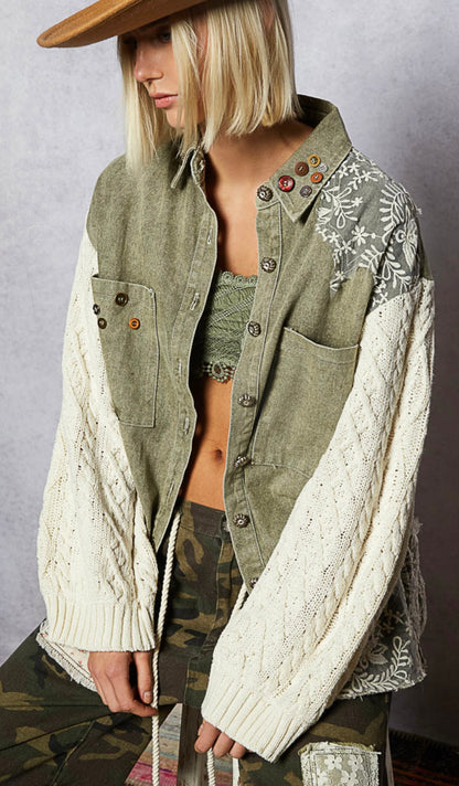 Person wearing a green jacket with white sleeves and floral embroidery, standing against a plain background.