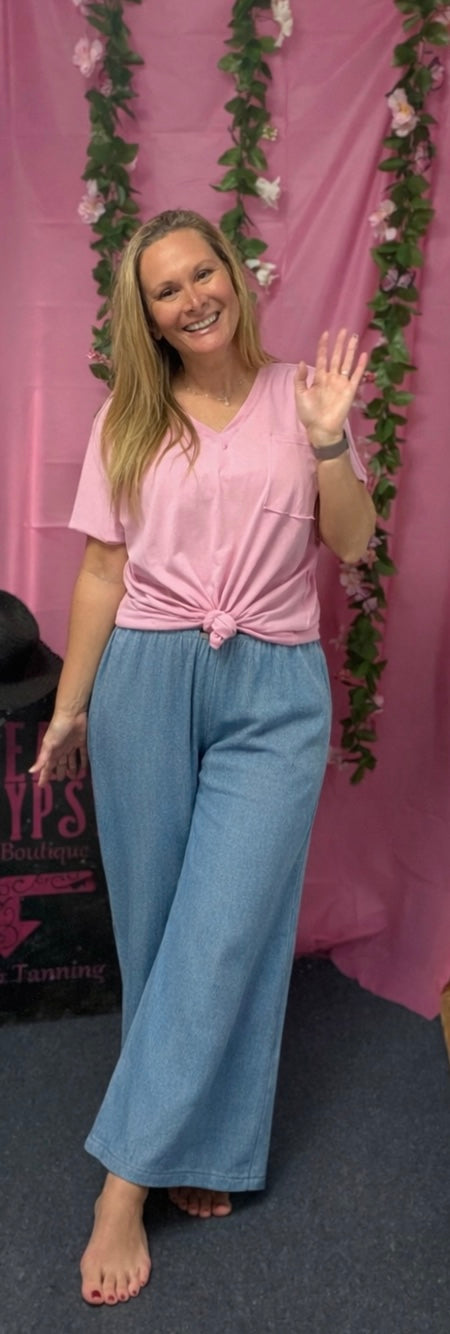 Woman in pink top and blue pants waving at a pink backdrop with floral decorations.
