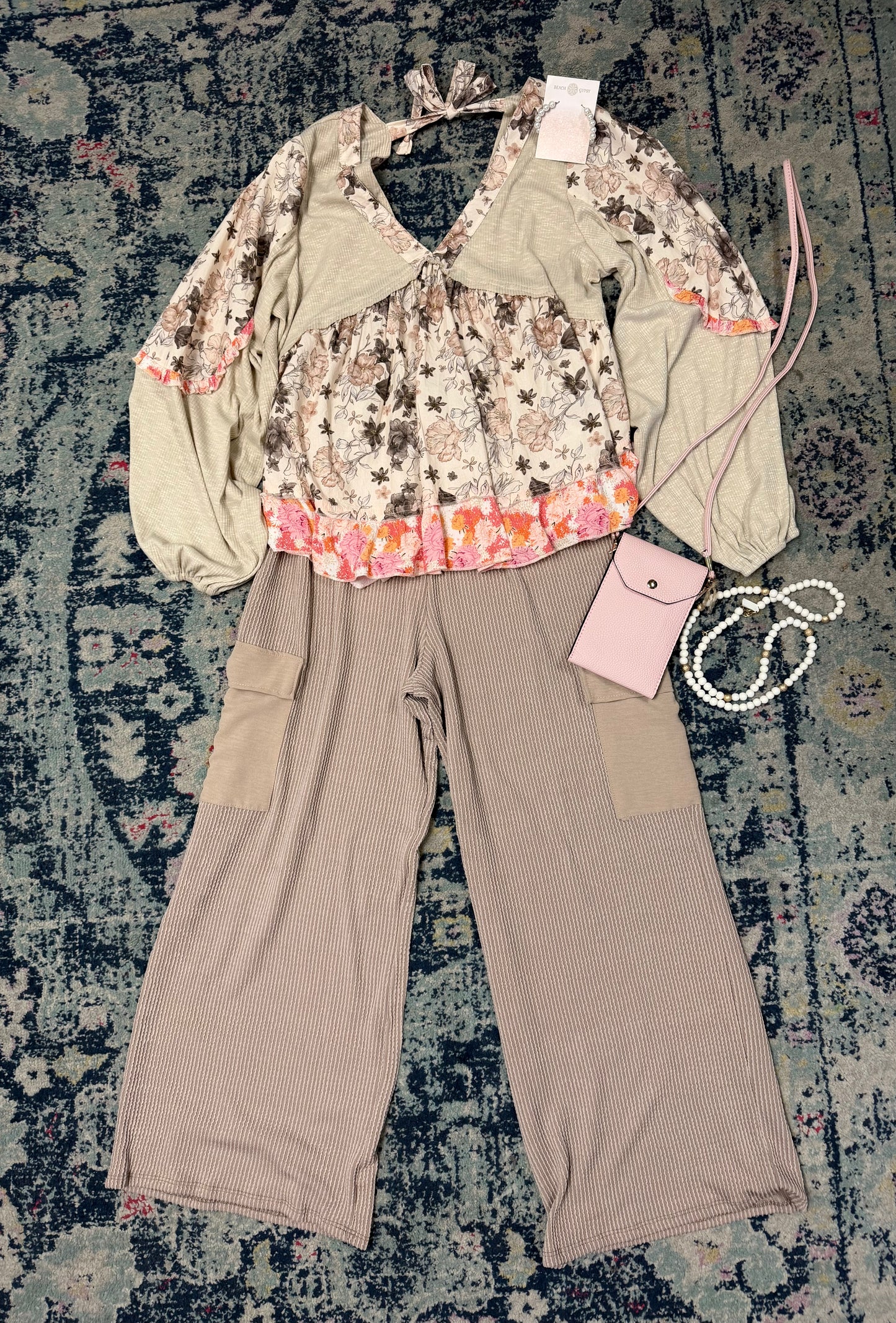 Fashion outfit with floral top and beige pants on a textured rug