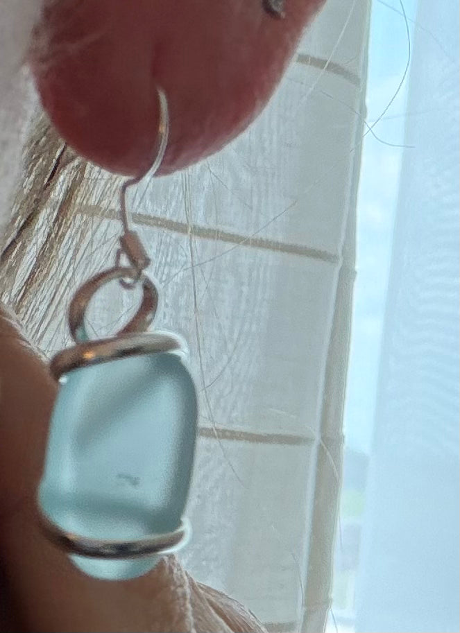 Light sea glass blue glass earring with silver setting held against a neutral background