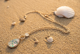 A long gold chain necklace with a teardrop-shaped iridescent abalone shell pendant