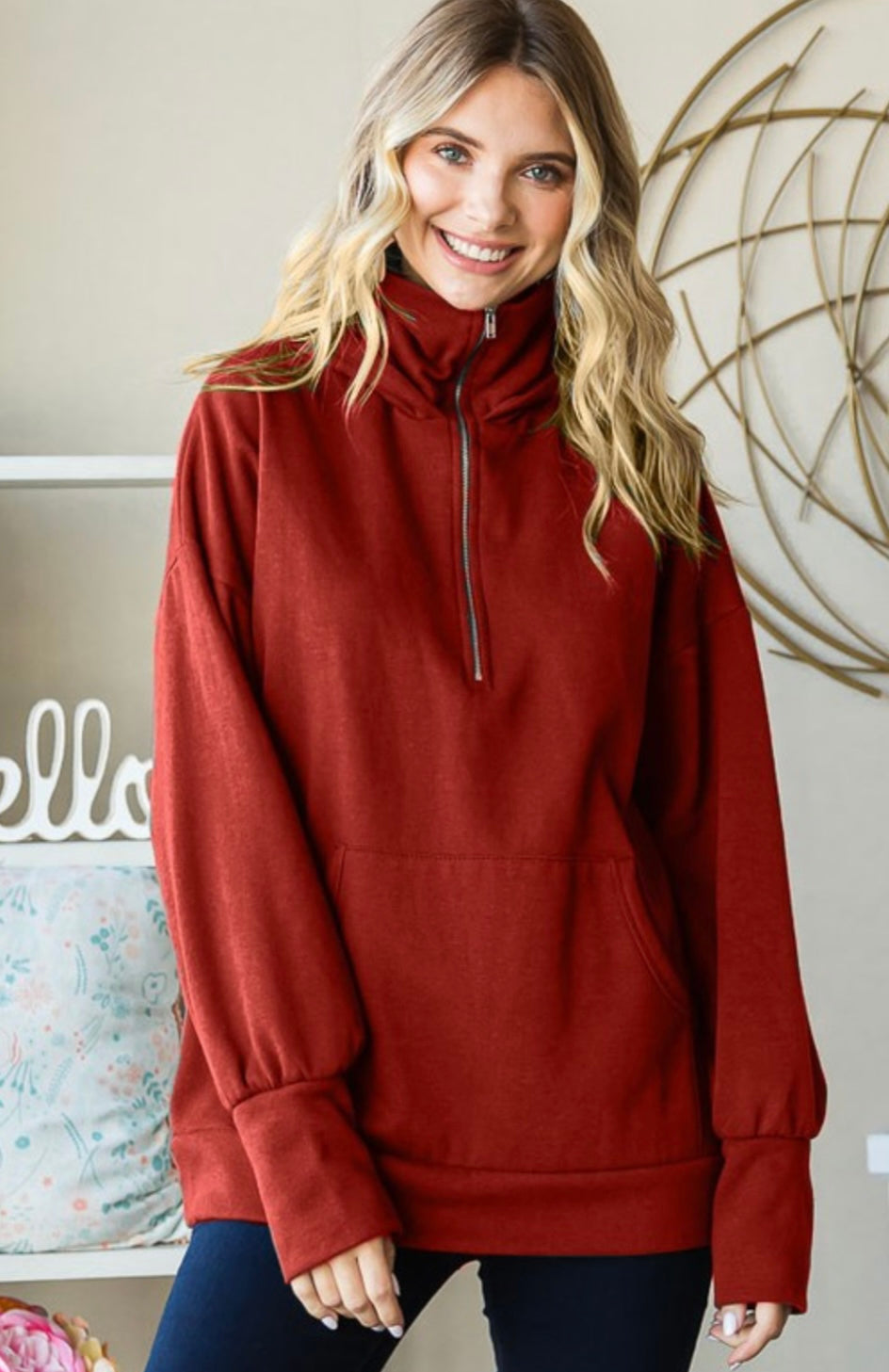 Woman wearing a red sweater with a high collar in a room with decorative elements.