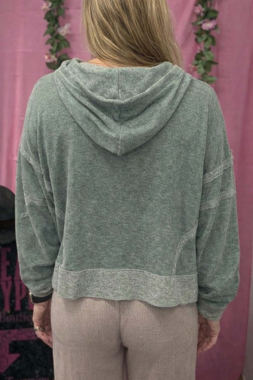Person wearing a green hoodie with a pink background