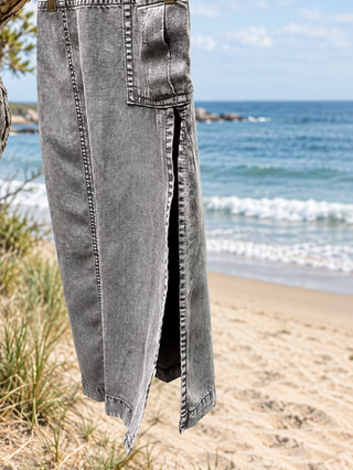 A close-up of a light gray washed denim garment, showing its texture and a side slit