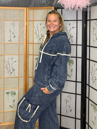 A woman wearing a dark blue denim matching set with white trim stands in a decorated room with folding screens and a pink feather hanging ornament.