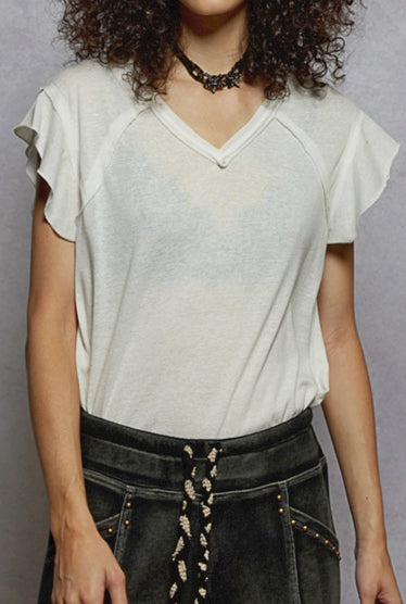 Person wearing a light-colored top and dark pants with decorative elements against a gray background