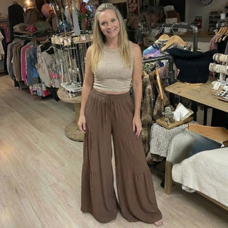 Woman wearing a beige top and brown wide-leg pants standing in a clothing store.