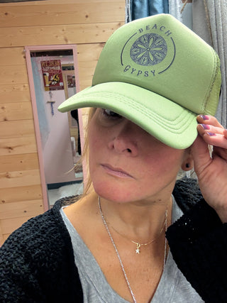 Green Beach Gypsy trucker hat on a woman in front of a wooden wall and mirror 