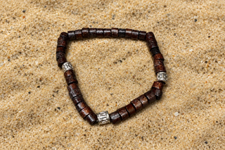 A beaded stretch bracelet made of dark brown cylindrical beads with three silver-toned spacer beads