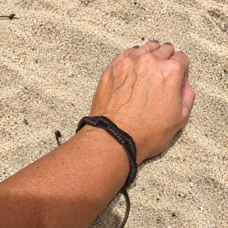 A close-up of a person's wrist wearing a dark brown braided cord bracelet