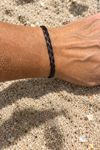 A dark brown braided cord bracelet worn on a person's wrist