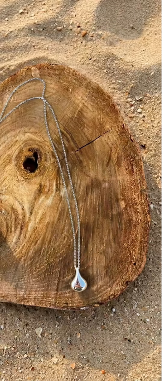 A silver-toned necklace with a small drop shaped pendant and a matching chain