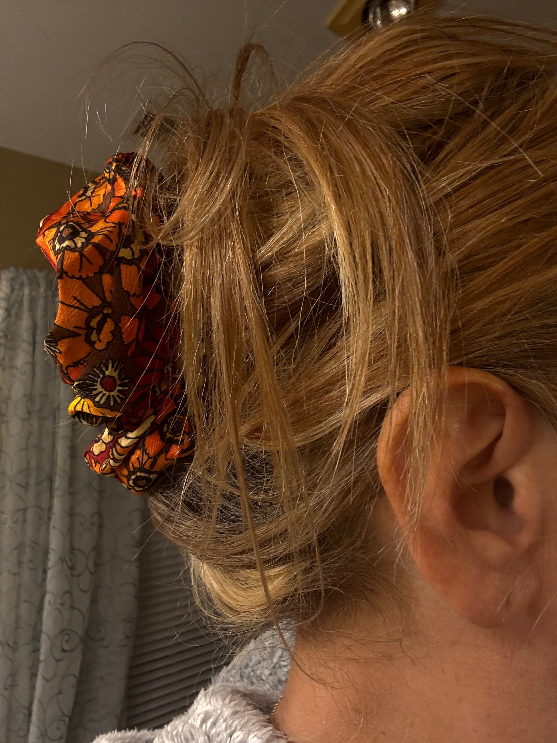 Close-up of a person's ear with a flower hair scrunchie in their hair.