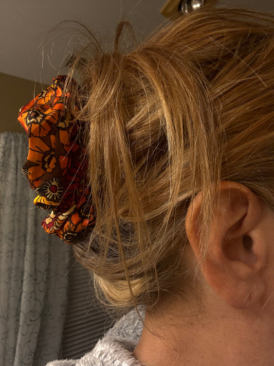 Close-up of a person's ear with a flower hair scrunchie in their hair.