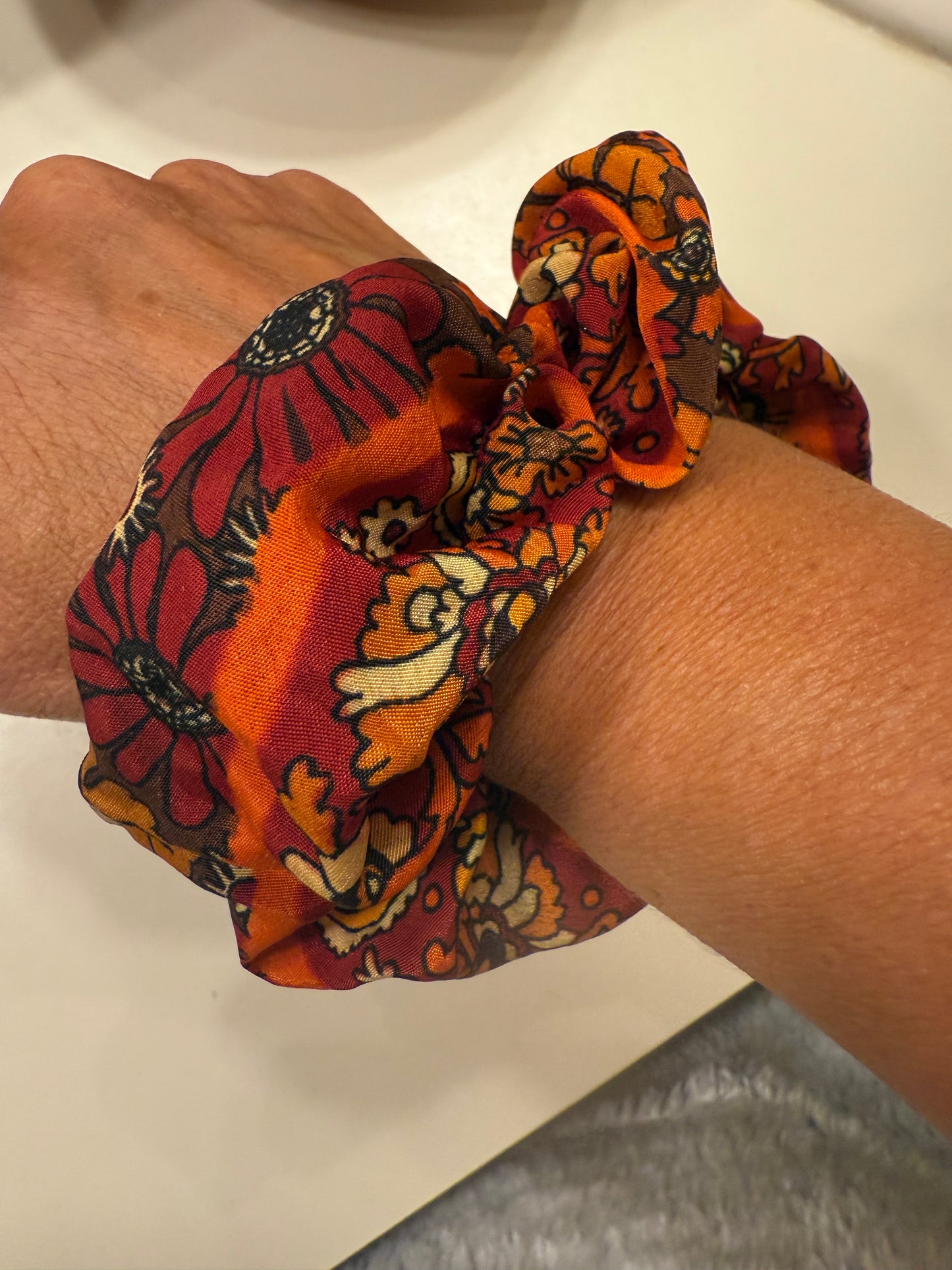 Hand wearing a colorful patterned scrunchie on a neutral background