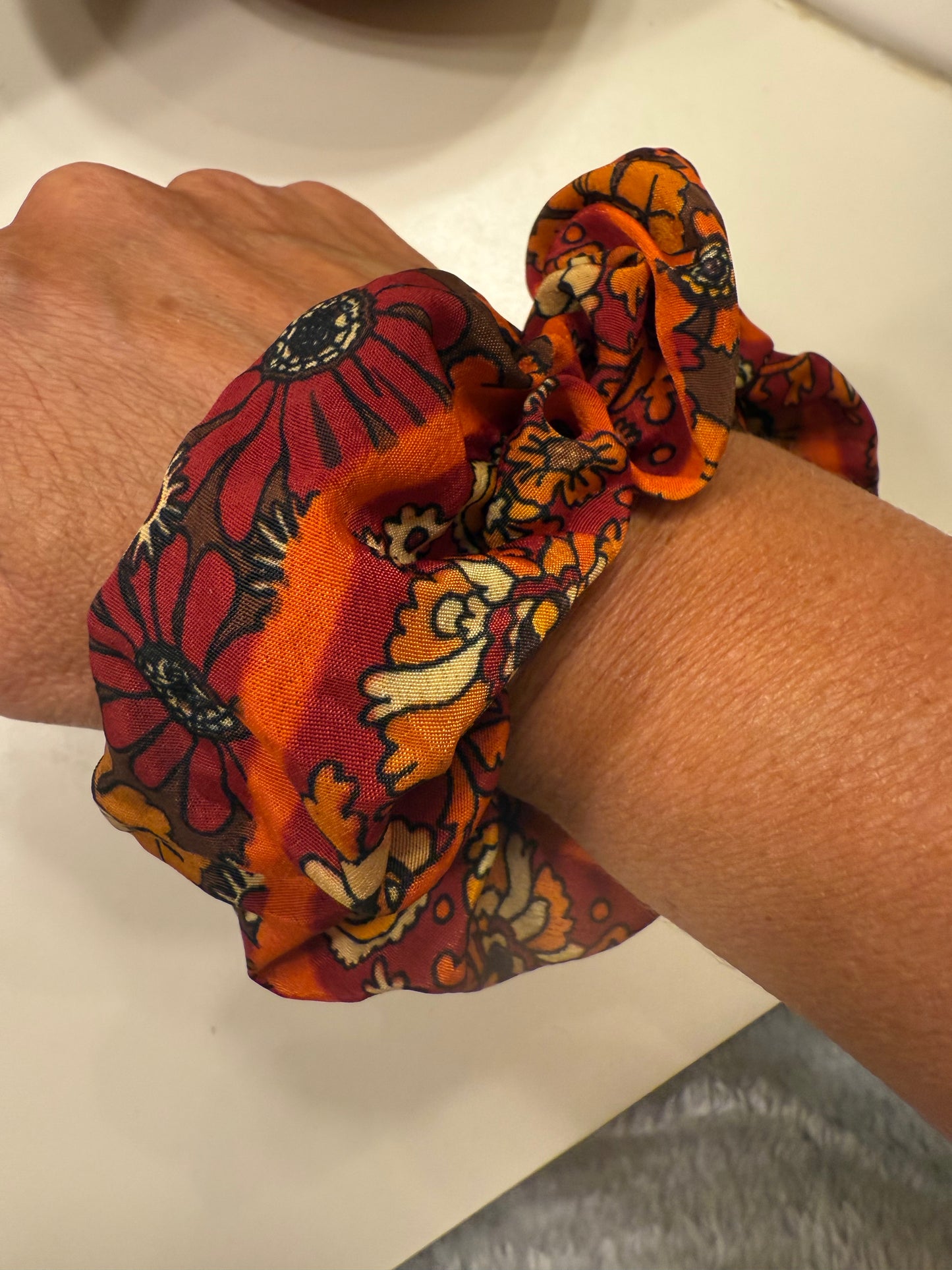Hand wearing a colorful floral-patterned scrunchie on a neutral background