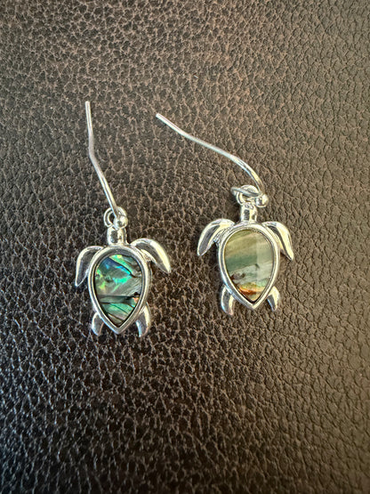 Silver turtle earrings with green stone on a brown textured surface