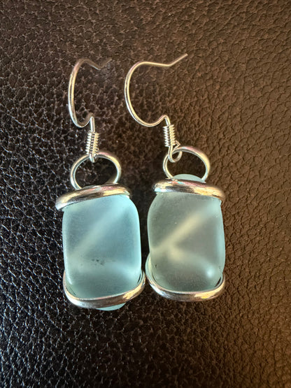 Pair of light blue glass earrings with silver settings on a brown textured background