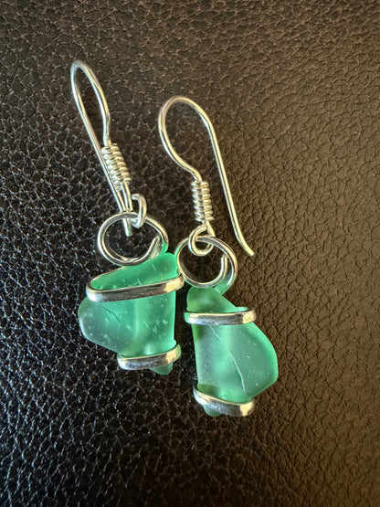 Green sea glass earrings with silver hooks on a dark brown leather background