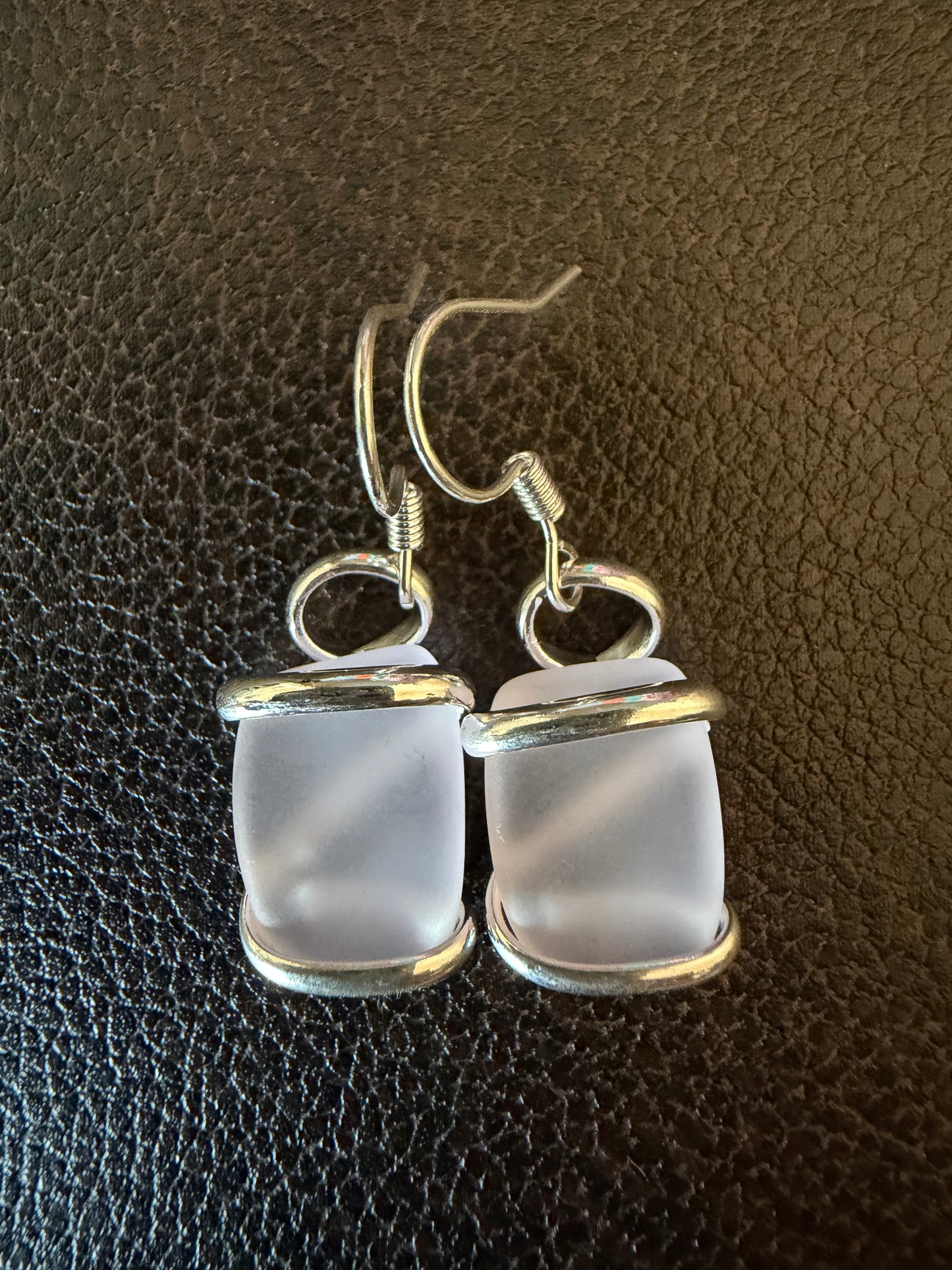 Pair of silver-framed pink sea glass earrings on a brown leather background