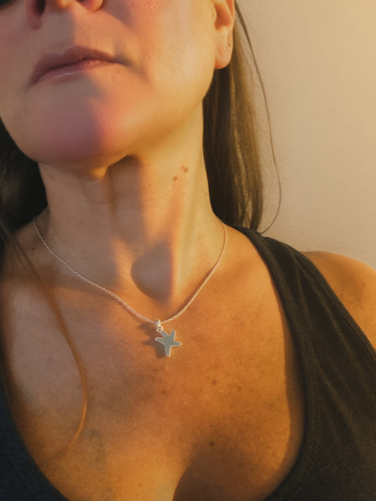 Close-up of a person wearing a starfish shaped necklace with warm lighting.
