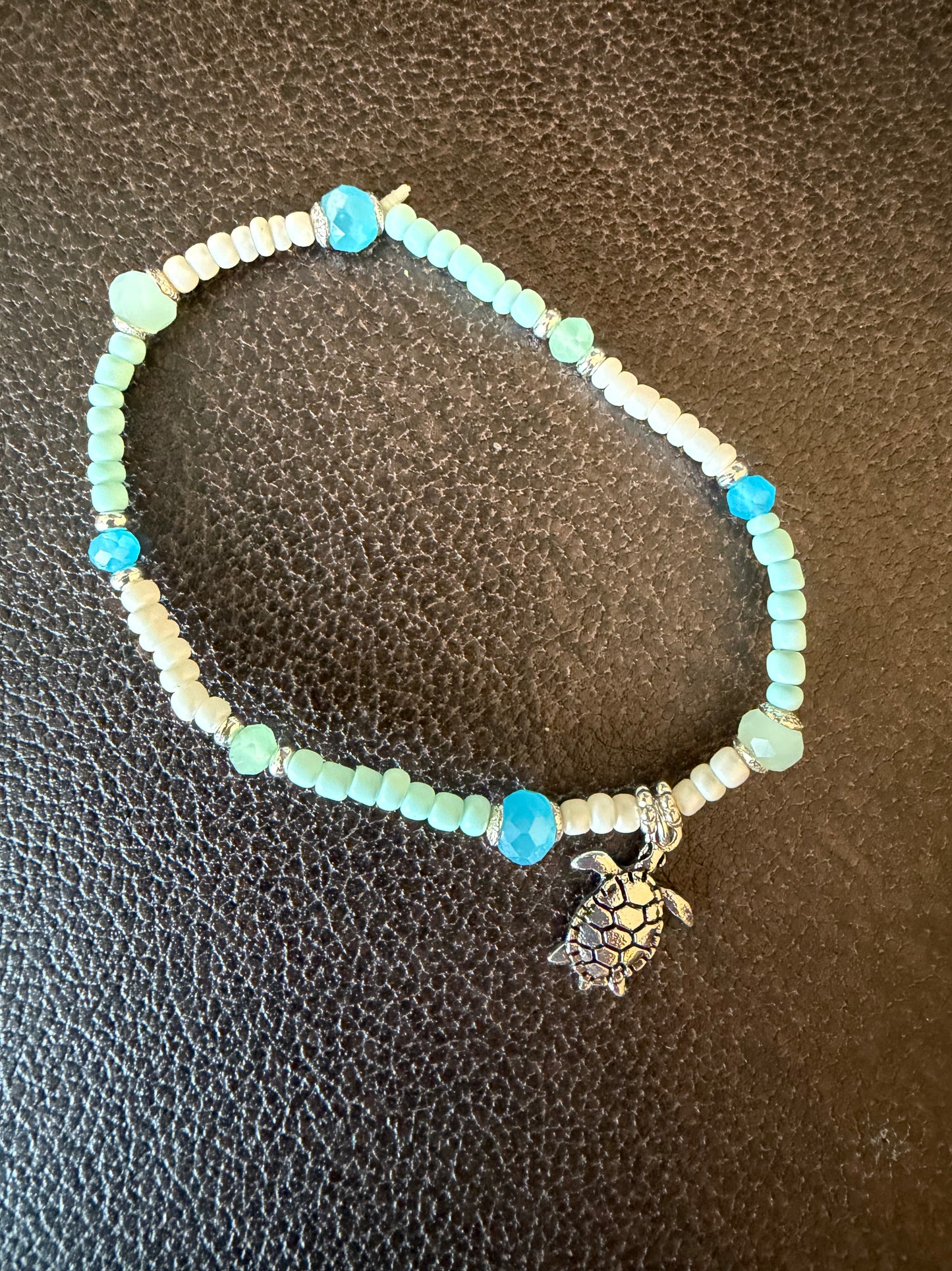 Beaded bracelet with a turtle charm on a textured brown surface