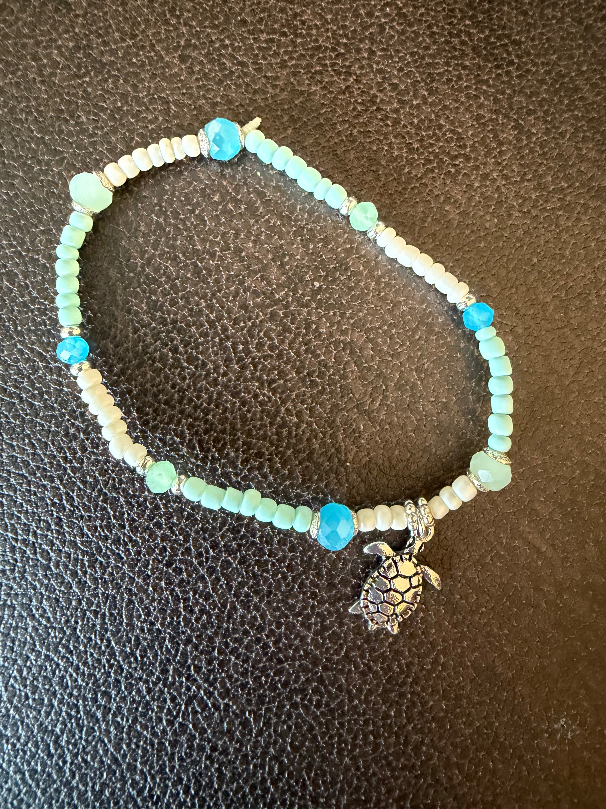 Beaded bracelet with a turtle charm on a textured brown surface