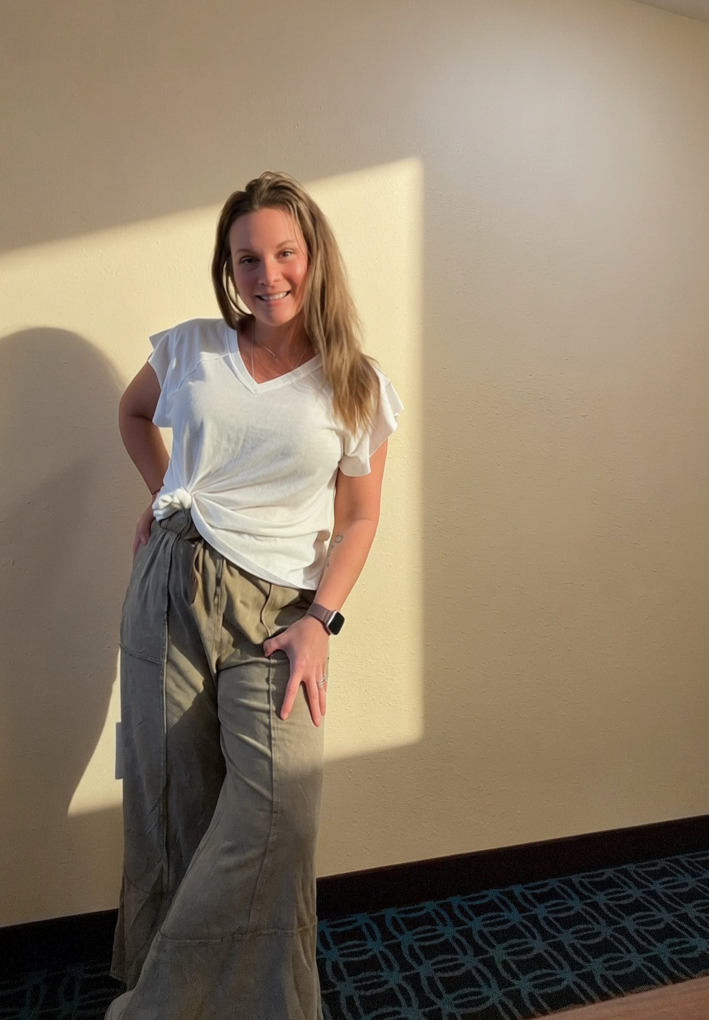 Woman wearing radian top against a beige wall with a light source casting a shadow on the wall.